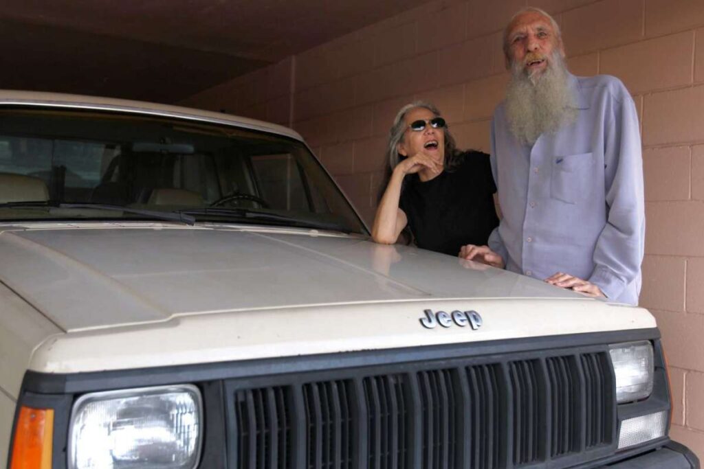 Elderly couple poses next to Jeep.