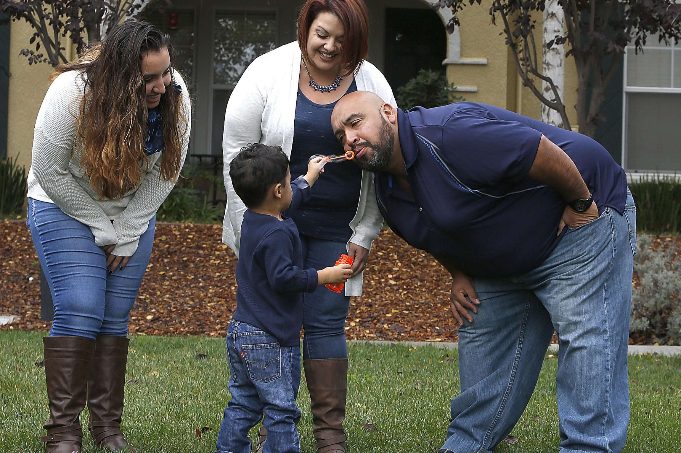 Family of four smiling together on the grass.