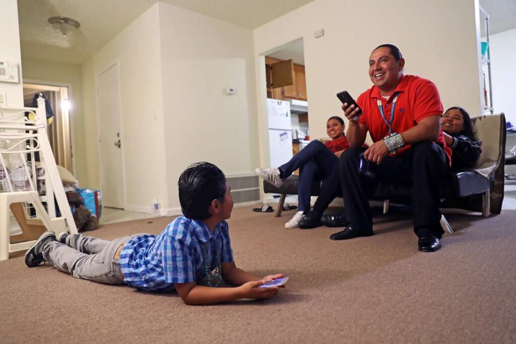 Adults and children sitting in a community room engaged in discussion.