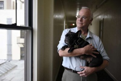 Man holding a small black dog inside a home.