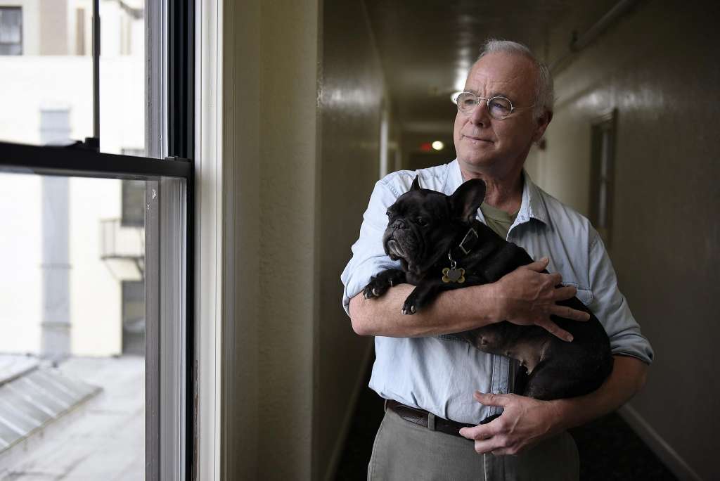 Man holding a small black dog inside a home.