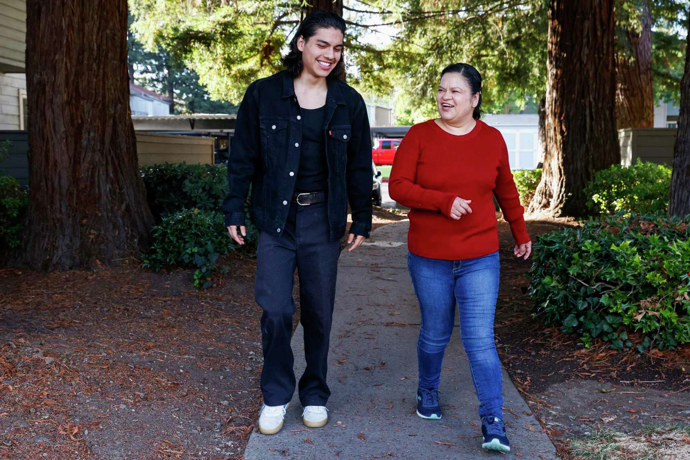 A mother and son walk together in a wooded area, smiling—suggesting family love and nature.