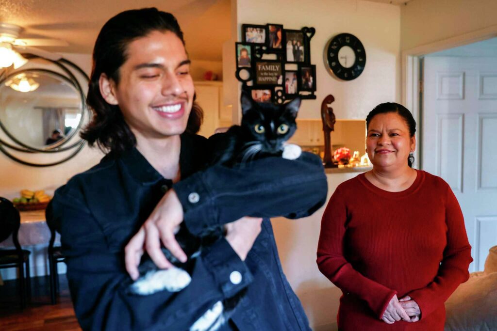 A young man and mother smile widely while holding a cat—capturing joy and connection.