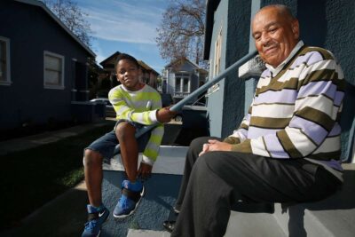 Elderly man and child sitting on a porch, smiling.