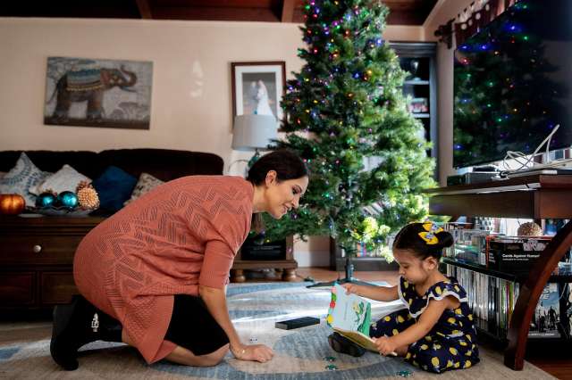 Mother and daughter read a book together near a Christmas tree.