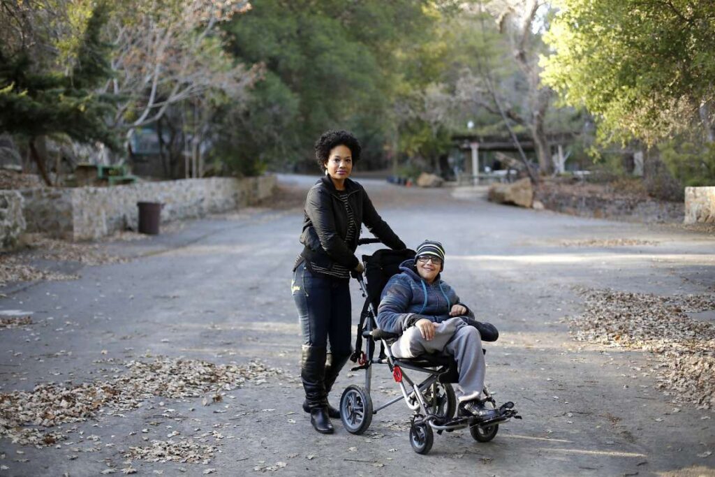 Mother poses with son in wheelchair at a park for a photo.