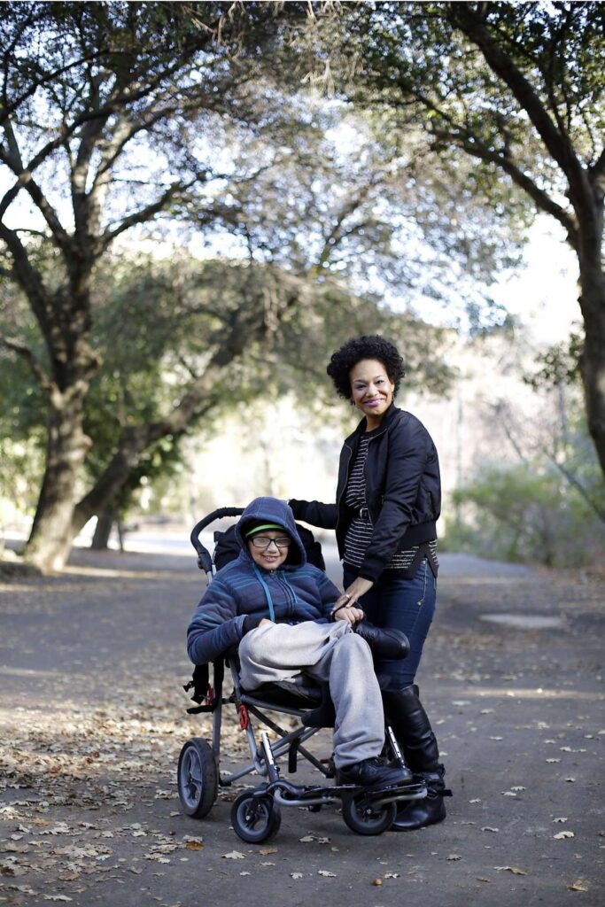 Mother poses with son in stroller for a photo at a park.