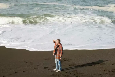 A man walks along the shoreline with waves in the background—evoking reflection and companionship.