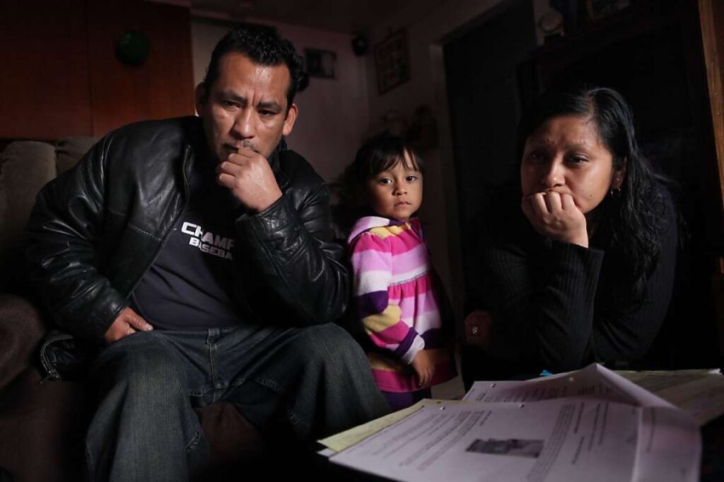 Family of three looking forlorn while sitting on couch.