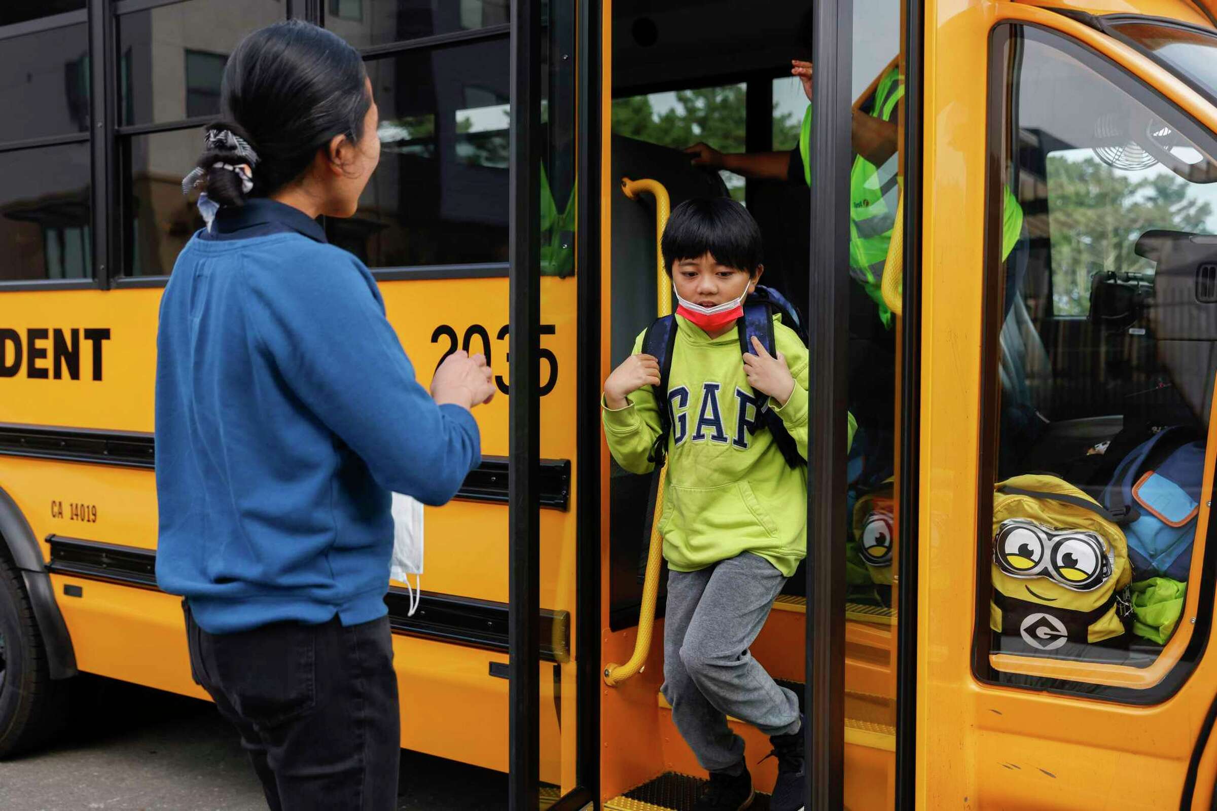 A child steps off a yellow school bus as mother waits—demonstrating care and support.
