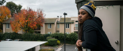 Woman looks out from apartment balcony.