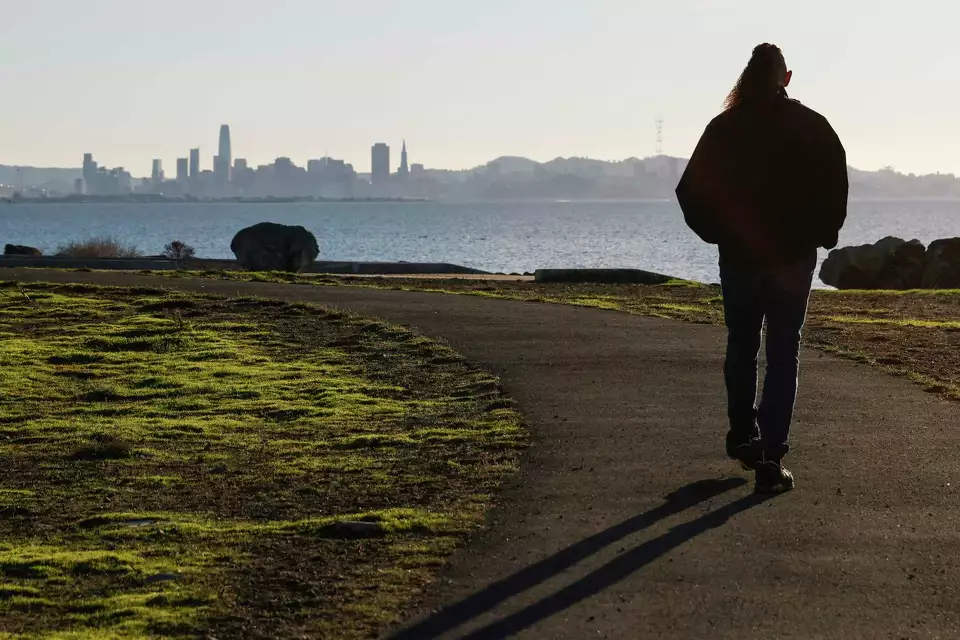 Silhouette of a man walking toward the water with a city view in the distance—conveying solitude, purpose, and journey.