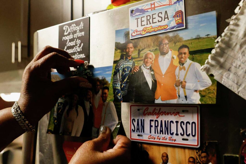 A hand holds a photo of a family beside a San Francisco sign—preserving family memories.