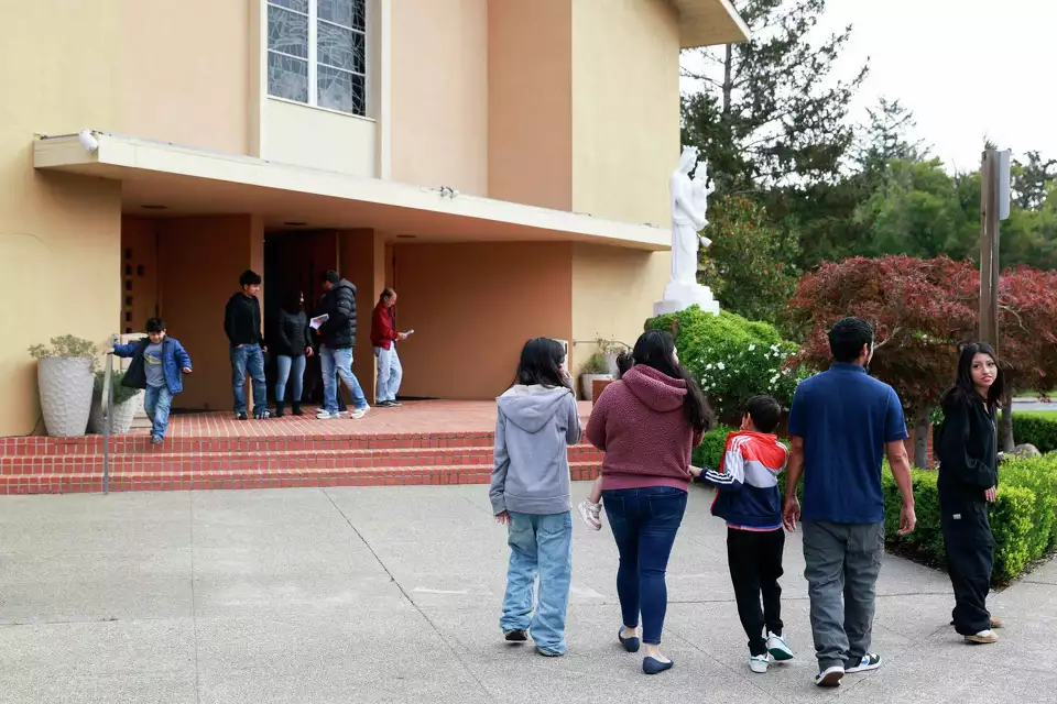A group of people walk toward entrance of a church, including adults and children—suggesting community gathering.