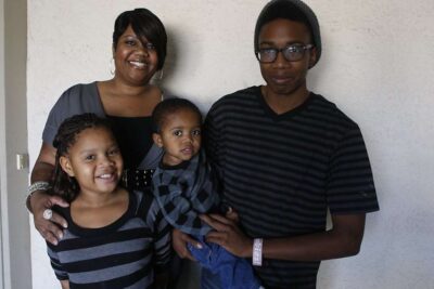 Family of four poses for photo outside home.