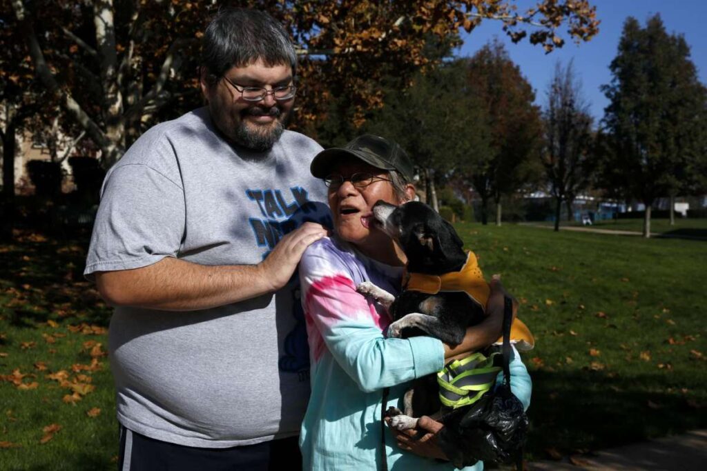 A couple hugs while holding small dog—capturing tenderness and joy.