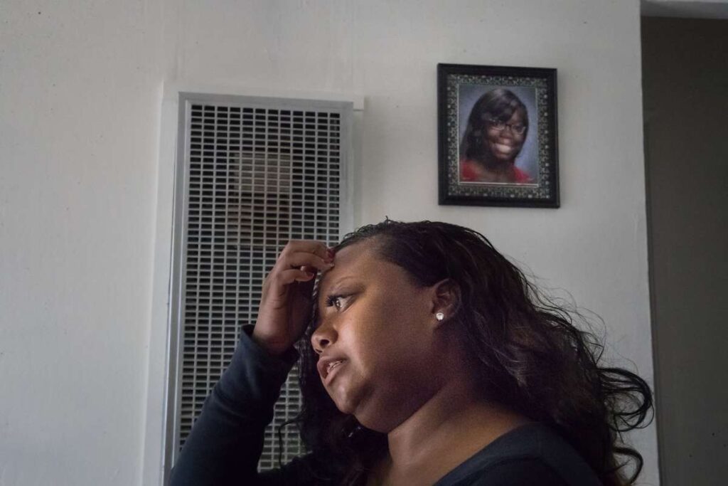 Woman standing in front of a wall inside a home, looking contemplative.