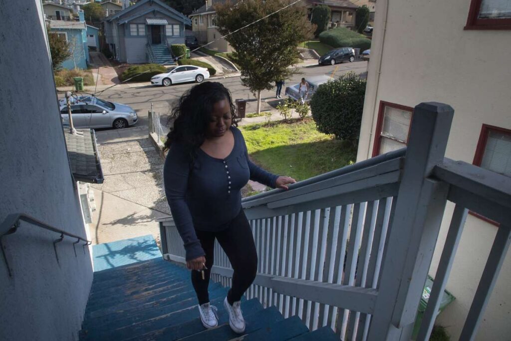 Woman walking up stairs to a front porch, holding onto the railing.