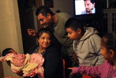 Family huddles around mother holding newborn baby.