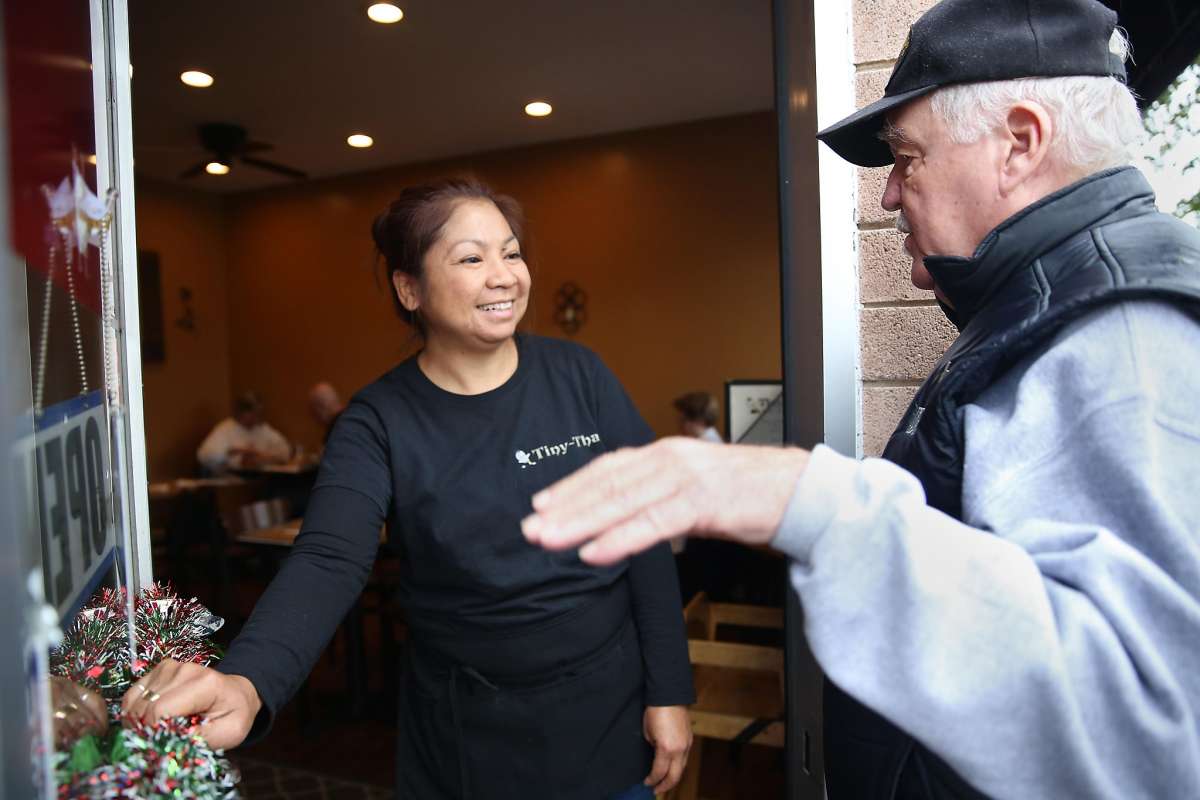 Restaurant worker greets elderly man outside entrance.