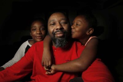 Two children kiss their father on his cheek for a photograph.