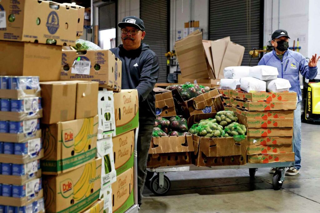 Volunteers load boxes of fresh produce into a vehicle—highlighting food distribution efforts.