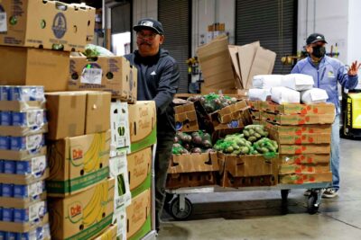 Volunteers load boxes of fresh produce into a vehicle—highlighting food distribution efforts.