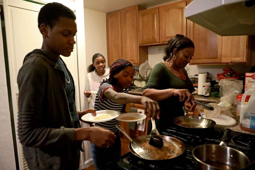 Family of four cooks dinner together in kitchen.