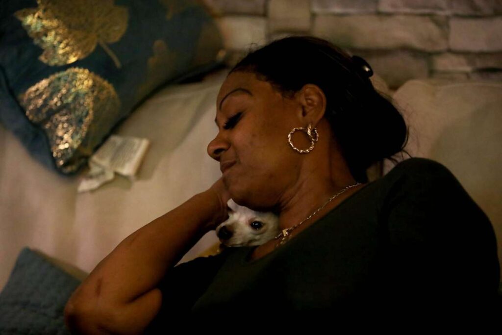 Woman cuddles with small dog on couch.