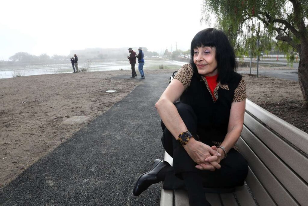 Woman sits on a park bench as others walk behind her.