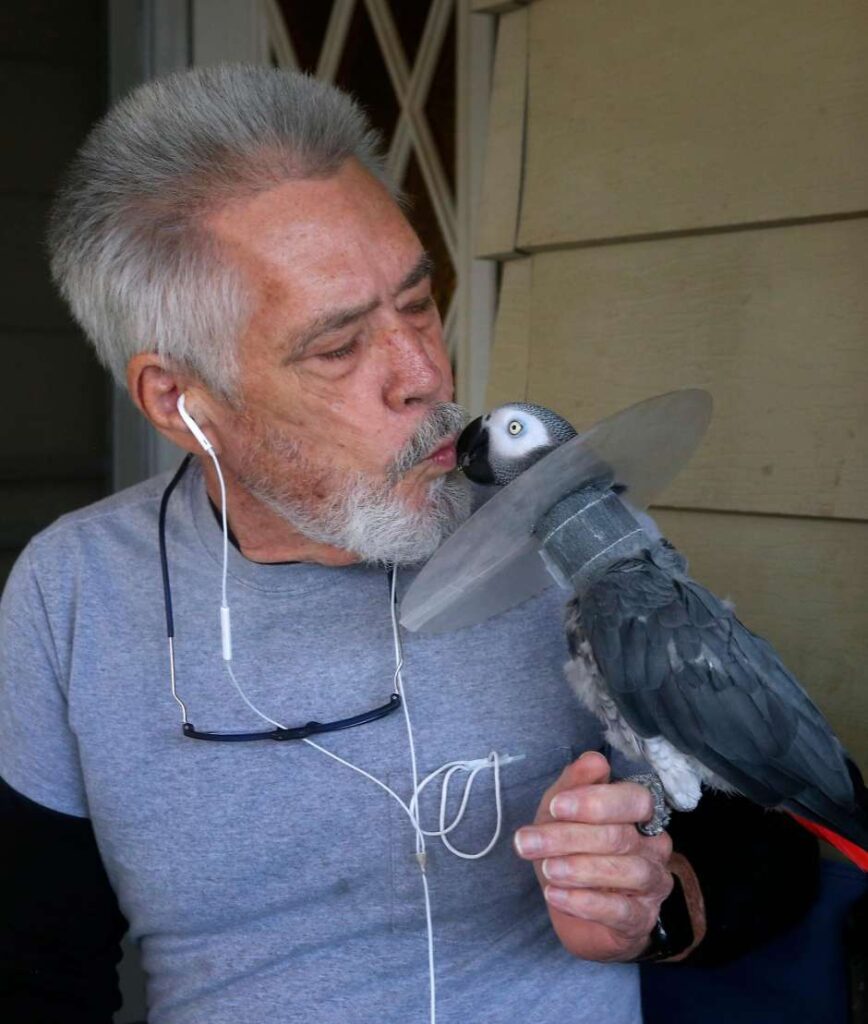 Man smiles as a parrot rests on his hand.