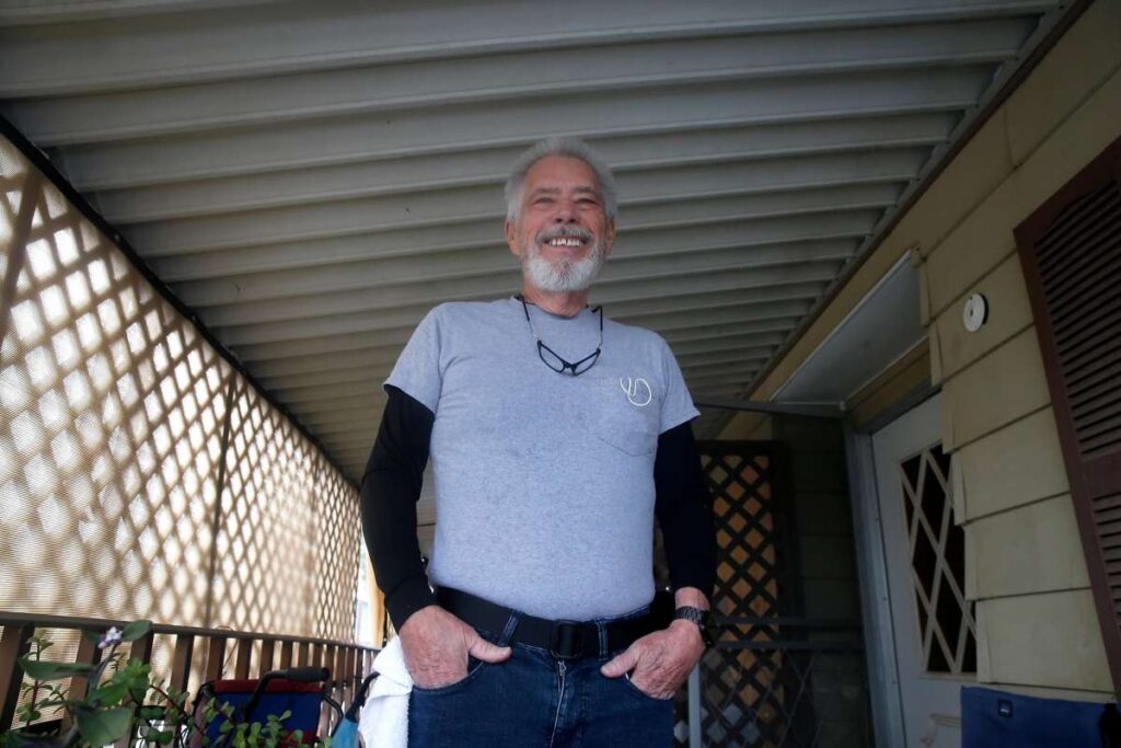 Older man stands confidently under a carport.