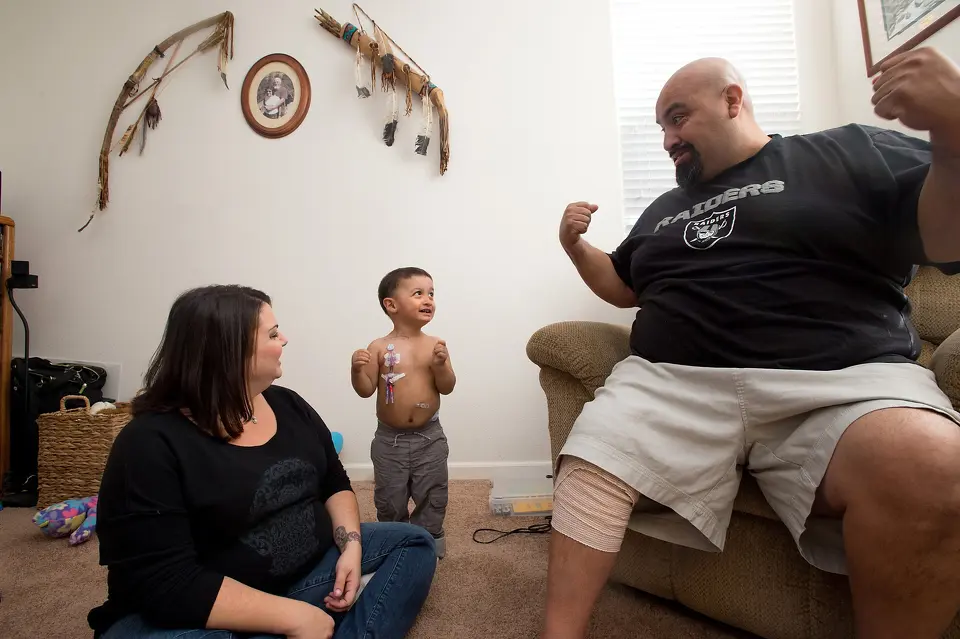 Parents encouraging child to smile in living room.
