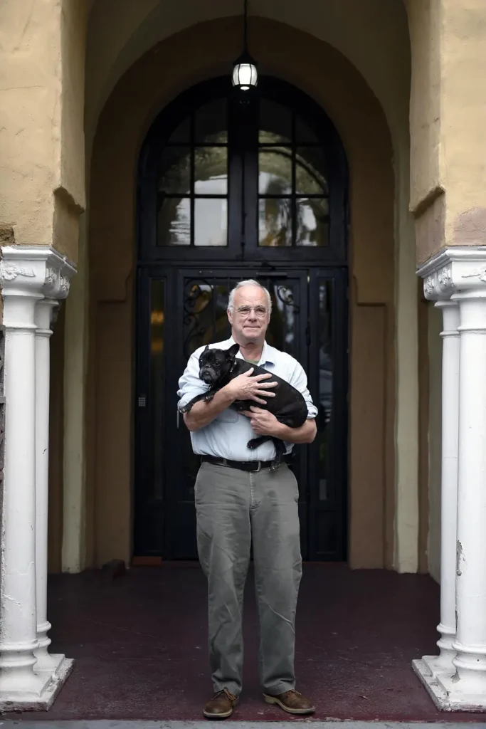 Elderly man holds dog in entryway of apartment building.